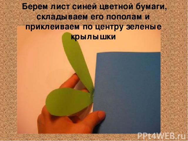  Берем лист синей цветной бумаги, складываем его пополам и приклеиваем по центру зеленые крылышки
